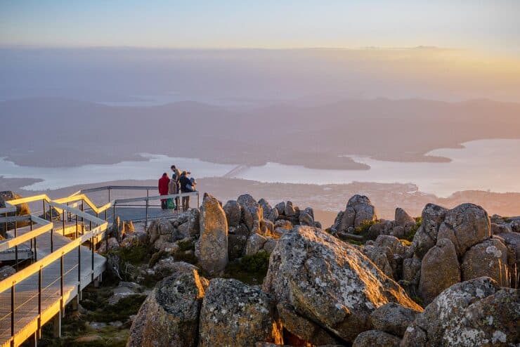 Group of people on a viewing platform watching a sunset over a coastal city landscape
